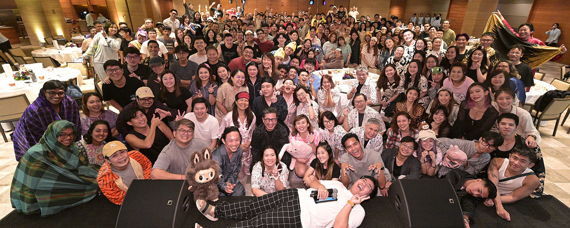 A group of people posing for a photo in a hotel ballroom in Singapore, wearing pajamas, for So Drama! Entertainment event.