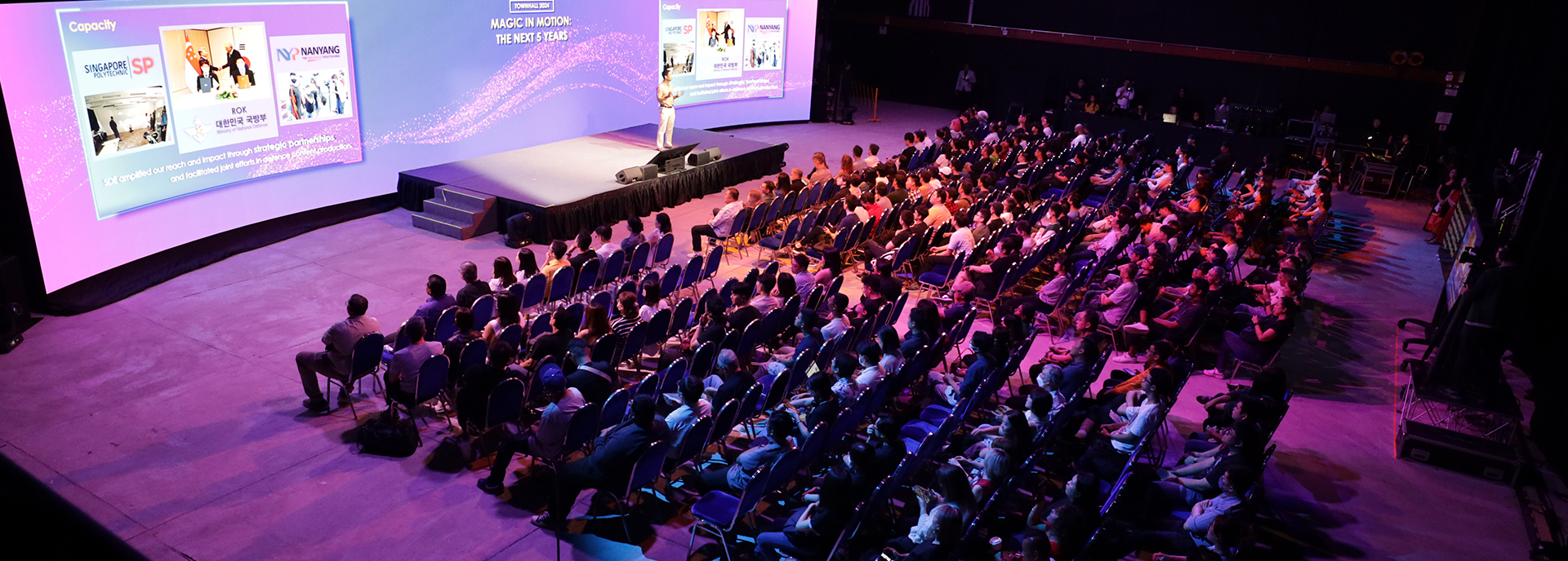 Speaker presenting on stage to a seated audience in an auditorium