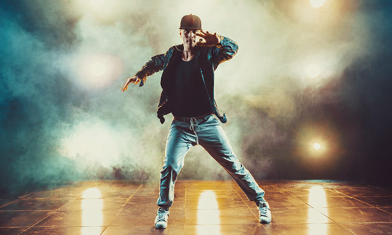 Young man breakdancing in a studio setting with heavy smoke and dramatic stage lighting.