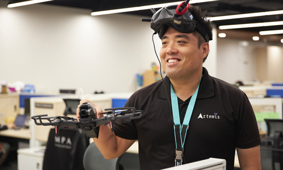 A person holding a small, four-propeller FPV (First Person View) drone, while wearing a set of FPV goggles.
